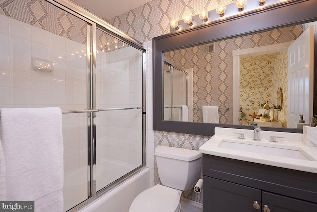 bathroom featuring enclosed tub / shower combo, toilet, vanity, and wallpapered walls