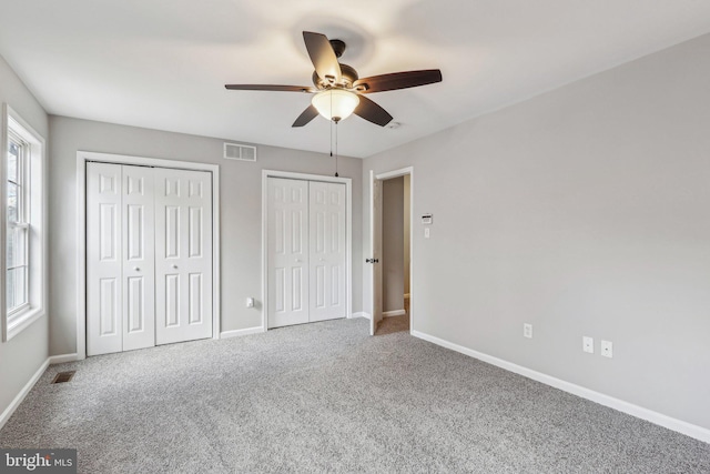 unfurnished bedroom with ceiling fan, carpet, and two closets