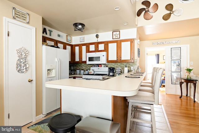 kitchen featuring white appliances, light hardwood / wood-style flooring, a kitchen breakfast bar, decorative backsplash, and kitchen peninsula