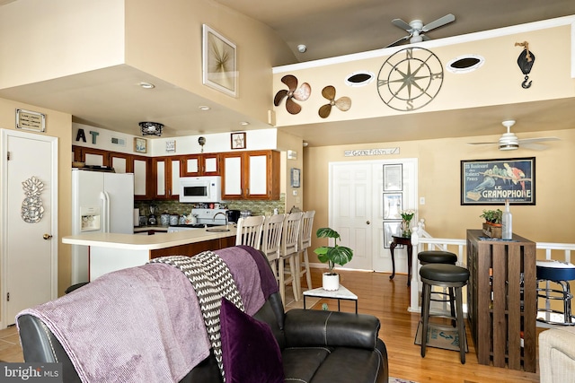 kitchen featuring white appliances, light hardwood / wood-style flooring, ceiling fan, decorative backsplash, and kitchen peninsula