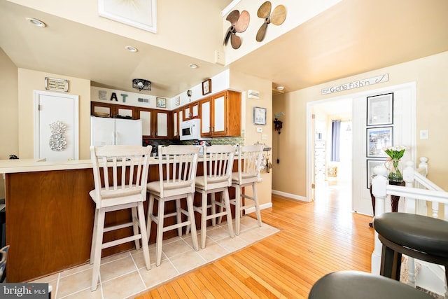 kitchen with white appliances, kitchen peninsula, and light wood-type flooring