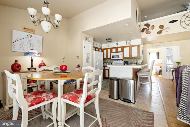 kitchen featuring a notable chandelier, light tile patterned floors, backsplash, and white appliances