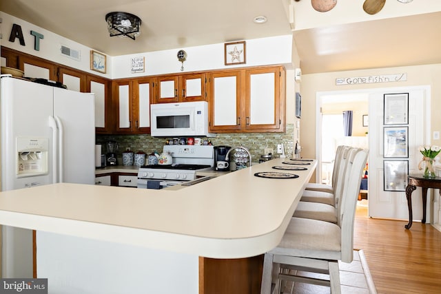 kitchen with light wood-type flooring, backsplash, white appliances, and kitchen peninsula