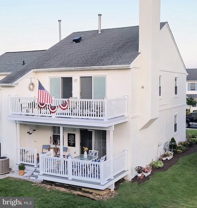 back house at dusk with cooling unit, a balcony, and a lawn