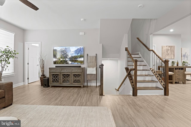 living room with baseboards, stairway, light wood-style flooring, and a ceiling fan