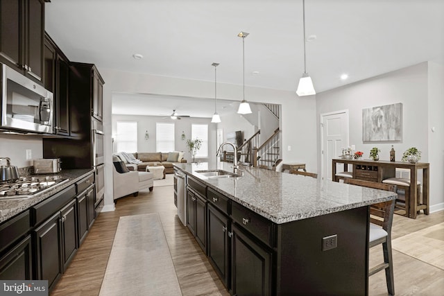 kitchen featuring appliances with stainless steel finishes, open floor plan, a kitchen island with sink, a sink, and a kitchen bar