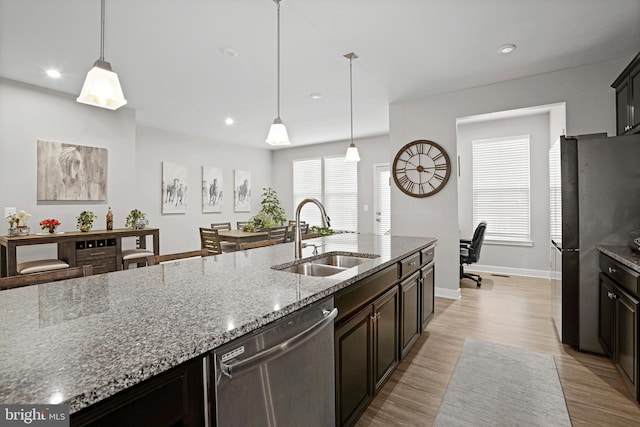 kitchen with light wood-style flooring, appliances with stainless steel finishes, light stone counters, hanging light fixtures, and a sink