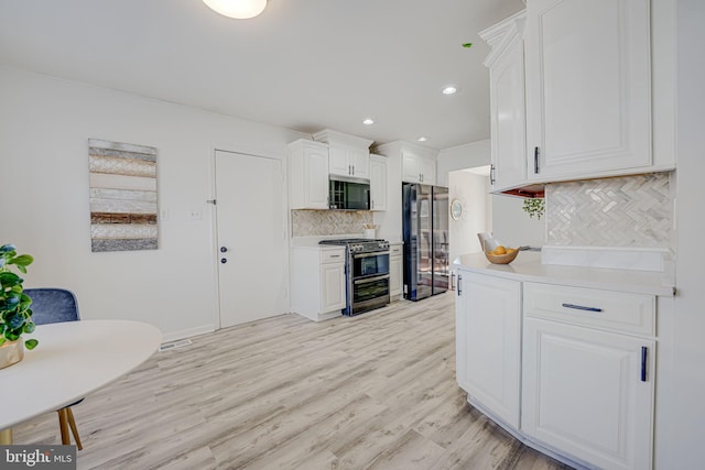 kitchen featuring stainless steel appliances, light countertops, light wood-type flooring, white cabinetry, and backsplash