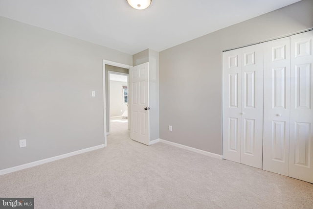 unfurnished bedroom featuring a closet, light colored carpet, and baseboards