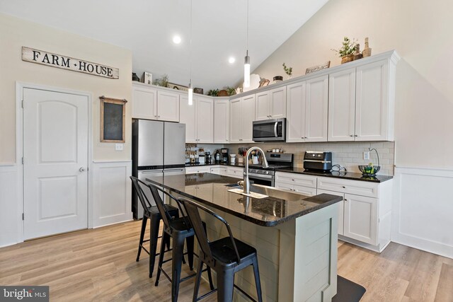 kitchen featuring vaulted ceiling, a center island with sink, dark stone counters, stainless steel appliances, and white cabinets