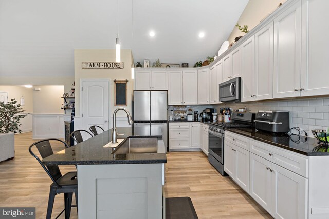 kitchen featuring appliances with stainless steel finishes, white cabinetry, sink, hanging light fixtures, and a kitchen island with sink