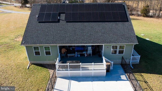 rear view of house featuring a wooden deck, a lawn, and solar panels