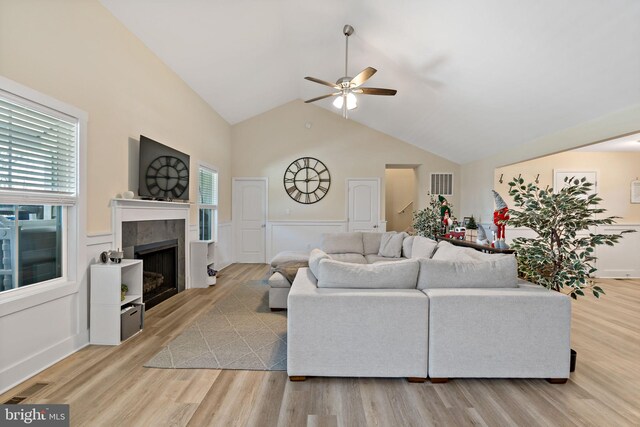 living room featuring high vaulted ceiling, a tile fireplace, ceiling fan, and light wood-type flooring