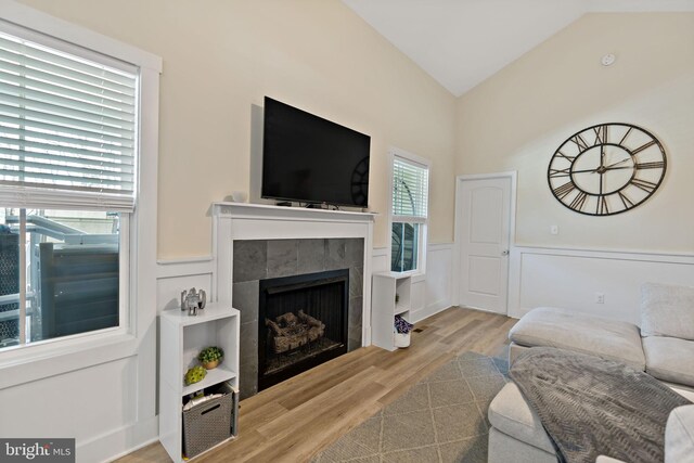 living room with lofted ceiling, a tiled fireplace, and light wood-type flooring