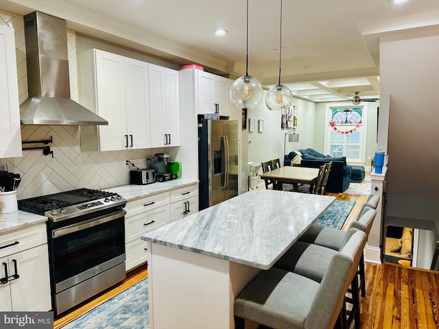 kitchen with a kitchen island, white cabinets, stainless steel appliances, light stone countertops, and wall chimney range hood