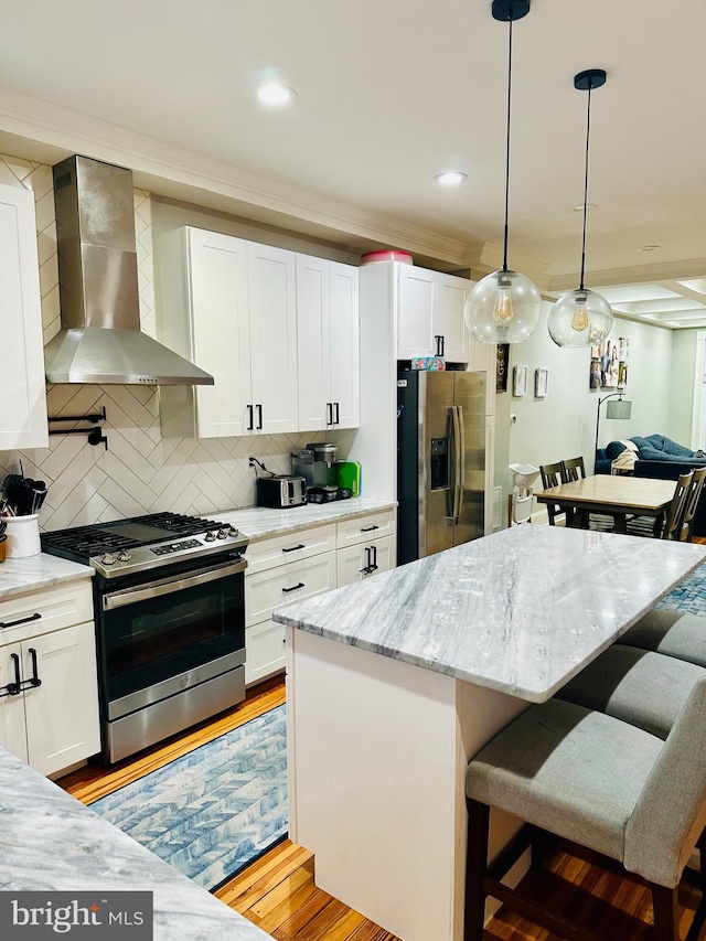 kitchen with white cabinets, appliances with stainless steel finishes, a kitchen island, and wall chimney range hood