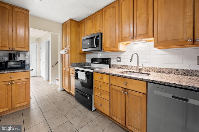 kitchen with sink, appliances with stainless steel finishes, tasteful backsplash, light stone countertops, and light tile patterned flooring