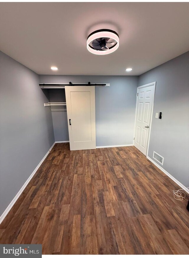 unfurnished bedroom featuring dark hardwood / wood-style floors and a barn door