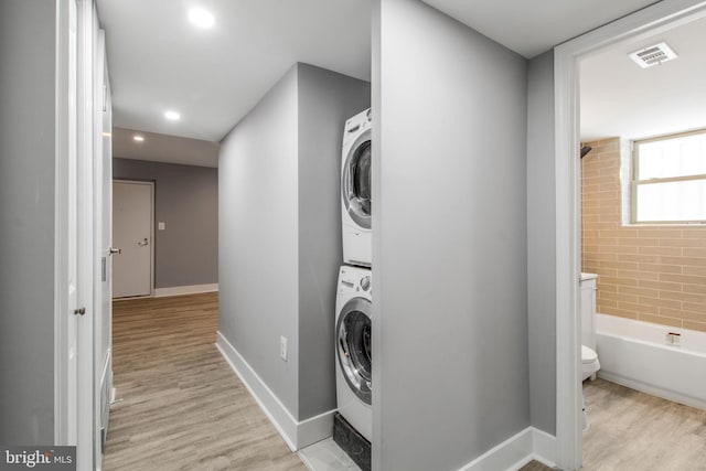 clothes washing area featuring stacked washer and clothes dryer and light wood-type flooring