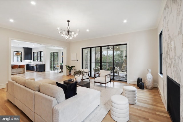 living room with a large fireplace, ornamental molding, a chandelier, and light wood-style floors