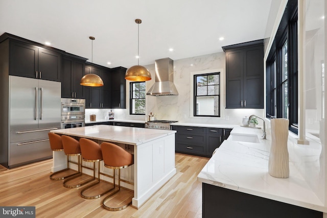 kitchen featuring a center island, stainless steel appliances, wall chimney range hood, pendant lighting, and a sink