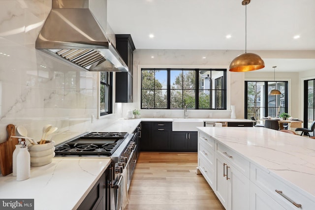 kitchen with range hood, decorative light fixtures, a sink, dark cabinets, and high end stove