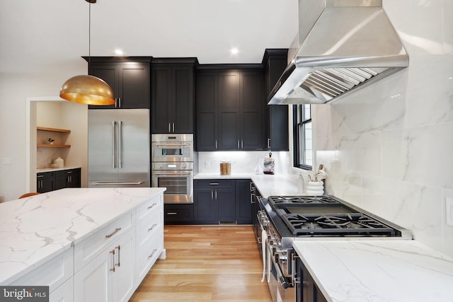 kitchen with high quality appliances, island exhaust hood, light stone counters, and decorative light fixtures