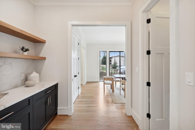 hallway featuring light wood-type flooring, crown molding, and baseboards