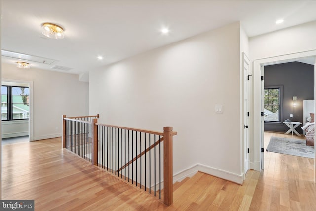 corridor with light wood-style floors, a wealth of natural light, visible vents, and an upstairs landing