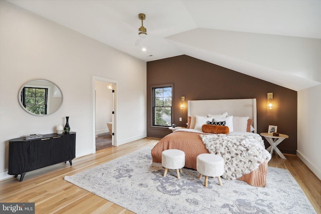 bedroom featuring lofted ceiling, ensuite bath, baseboards, and wood finished floors