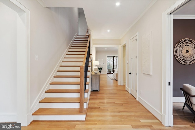 entrance foyer with baseboards, crown molding, light wood finished floors, and stairs