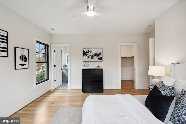 bedroom with light wood-style flooring, a spacious closet, baseboards, and a ceiling fan