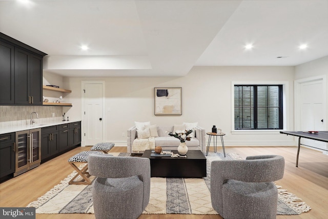 living room featuring light wood-type flooring, wine cooler, baseboards, and wet bar