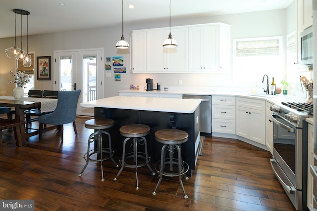 kitchen featuring sink, appliances with stainless steel finishes, white cabinetry, a kitchen island, and decorative light fixtures