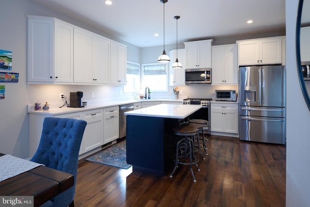 kitchen with a kitchen island, appliances with stainless steel finishes, pendant lighting, white cabinetry, and dark hardwood / wood-style flooring