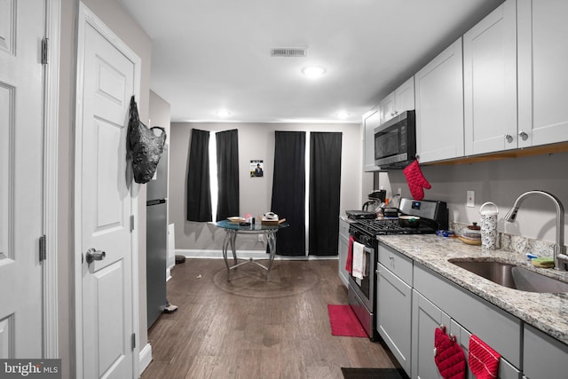 kitchen featuring dark wood-type flooring, sink, light stone counters, white cabinetry, and stainless steel appliances