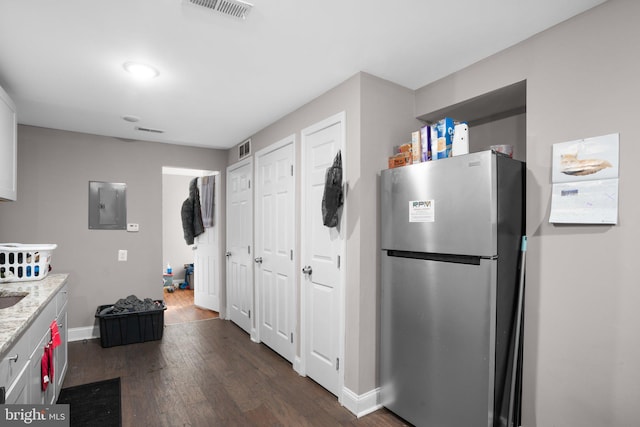 kitchen with dark wood-type flooring, light stone counters, stainless steel fridge, electric panel, and white cabinets