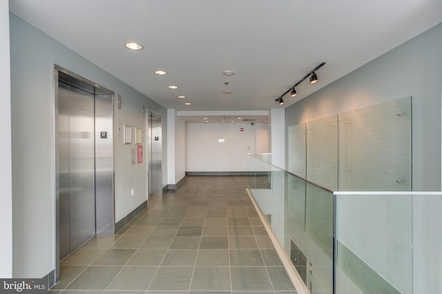 corridor with elevator, rail lighting, and light tile patterned floors