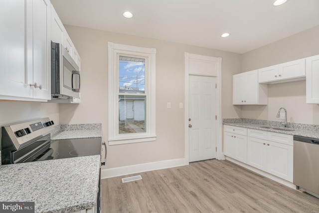 kitchen with stainless steel appliances, white cabinetry, light stone countertops, and sink