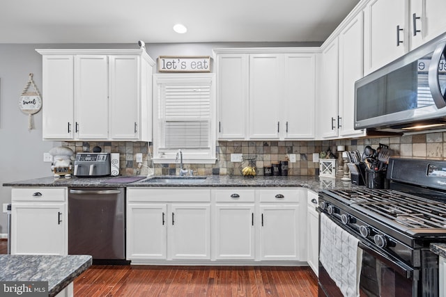 kitchen with appliances with stainless steel finishes, sink, dark stone counters, and white cabinets