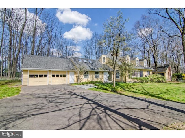 cape cod-style house featuring an attached garage, aphalt driveway, and a front yard