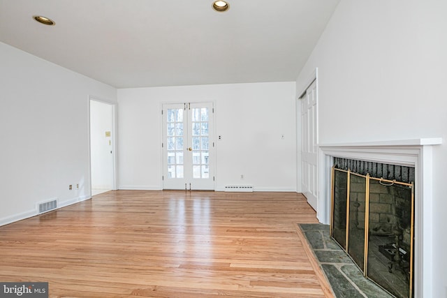 unfurnished living room featuring visible vents, baseboards, a fireplace with flush hearth, light wood-type flooring, and a baseboard heating unit