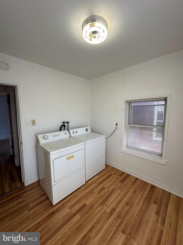 clothes washing area with washing machine and clothes dryer and light wood-type flooring