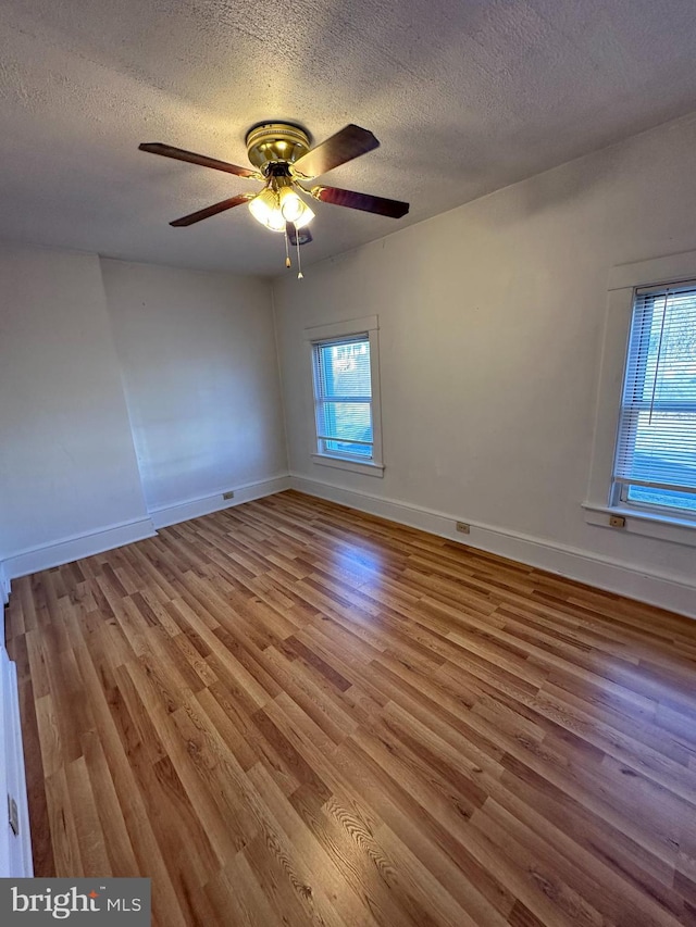 empty room featuring ceiling fan, light hardwood / wood-style floors, a textured ceiling, and a wealth of natural light