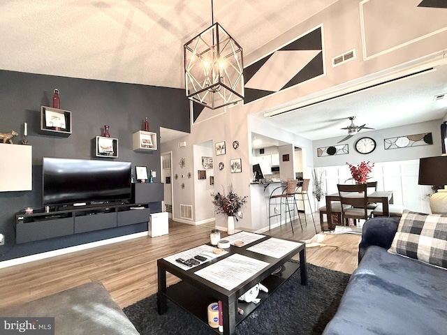 living room featuring hardwood / wood-style floors, ceiling fan with notable chandelier, and vaulted ceiling