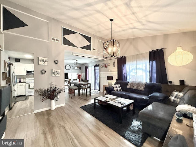 living room with an inviting chandelier, high vaulted ceiling, light hardwood / wood-style floors, and a wealth of natural light