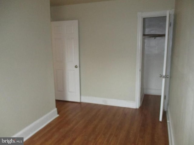 unfurnished bedroom featuring a walk in closet, dark hardwood / wood-style flooring, and a closet