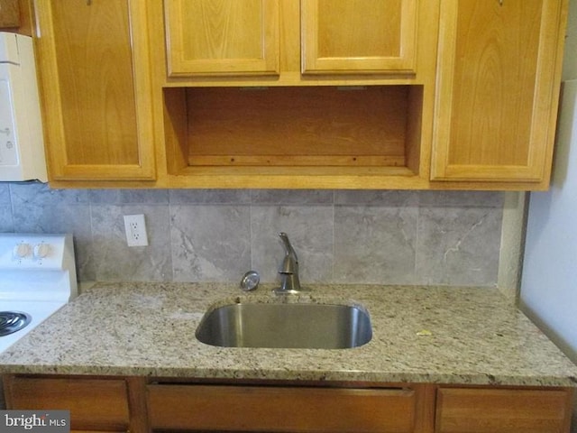 kitchen featuring tasteful backsplash, light stone countertops, stove, and sink