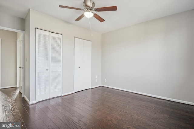 unfurnished bedroom with baseboards, dark wood-type flooring, multiple closets, and a ceiling fan