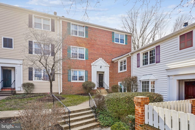 view of front of home featuring brick siding, entry steps, and fence